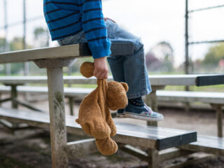 sad child sitting on bleachers with his stuffed bear